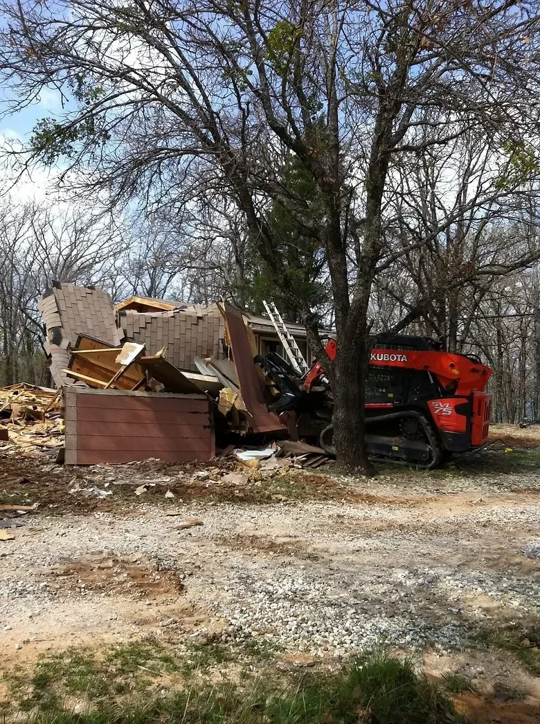 Demolition equipment removing roofing materials and structural debris from residential building