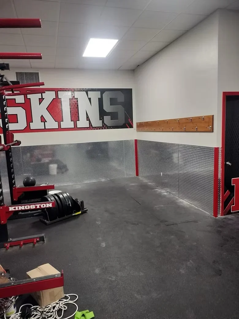 Polished concrete floor with metal mesh wall panels and red steel framing in athletic facility