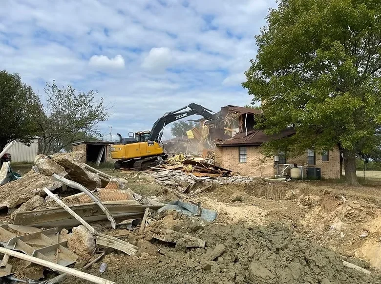 Excavator demolishing brick building with debris and rubble scattered on site
