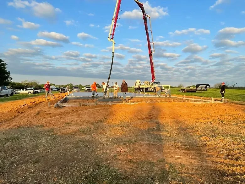 Concrete foundation pour with two pump trucks delivering concrete to elevated pad on prepared site