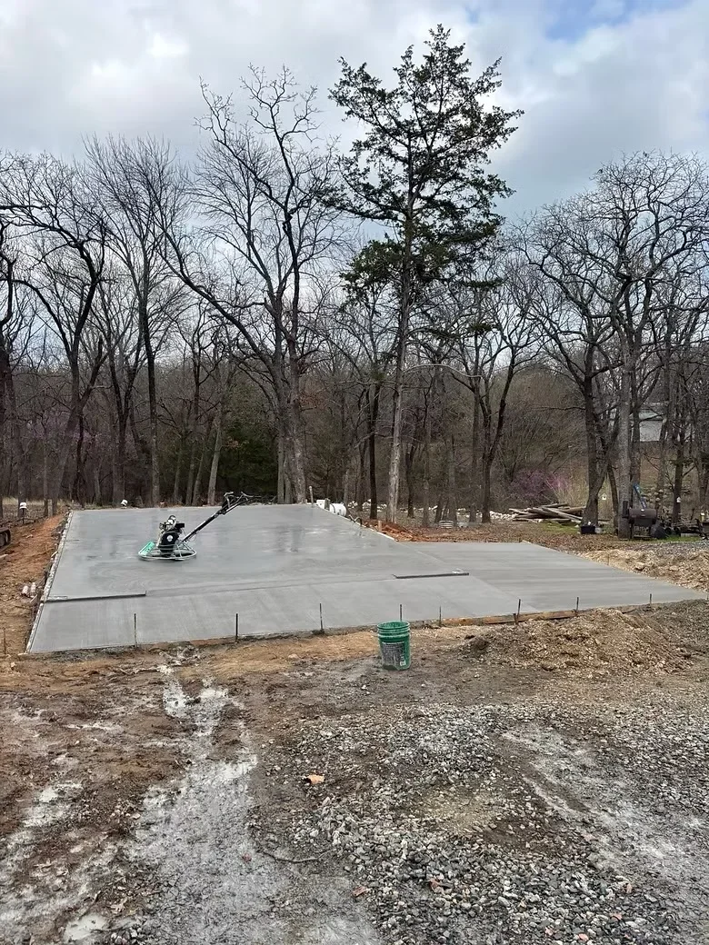 Freshly poured concrete pad with control joints, gravel base, and power finishing equipment on site