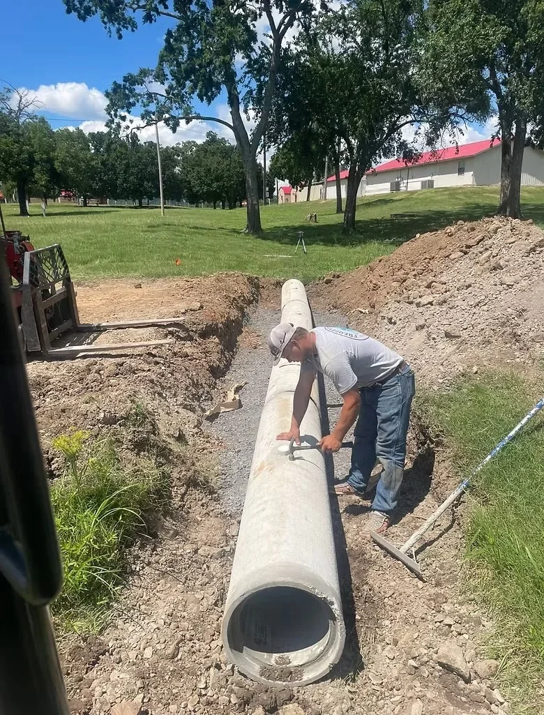 Concrete drainage pipe installation in trench with crew positioning large-diameter pipe