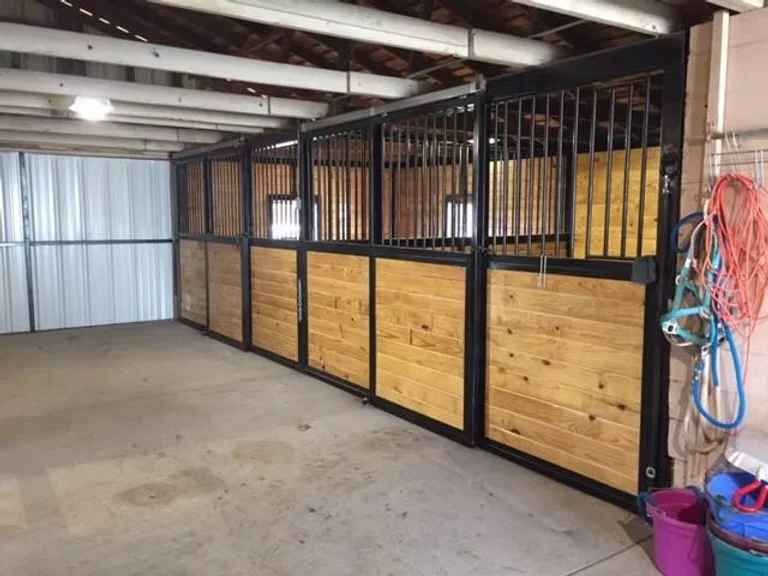 Concrete barn floor with metal-framed wooden horse stalls and overhead lighting