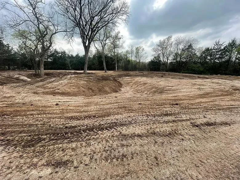 Graded dirt lot with mature trees, prepared subgrade for concrete work