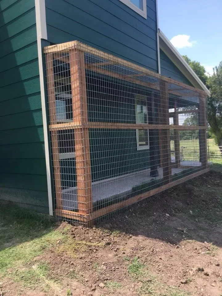 Brick-framed animal enclosure with wire mesh panels and concrete base attached to residential building
