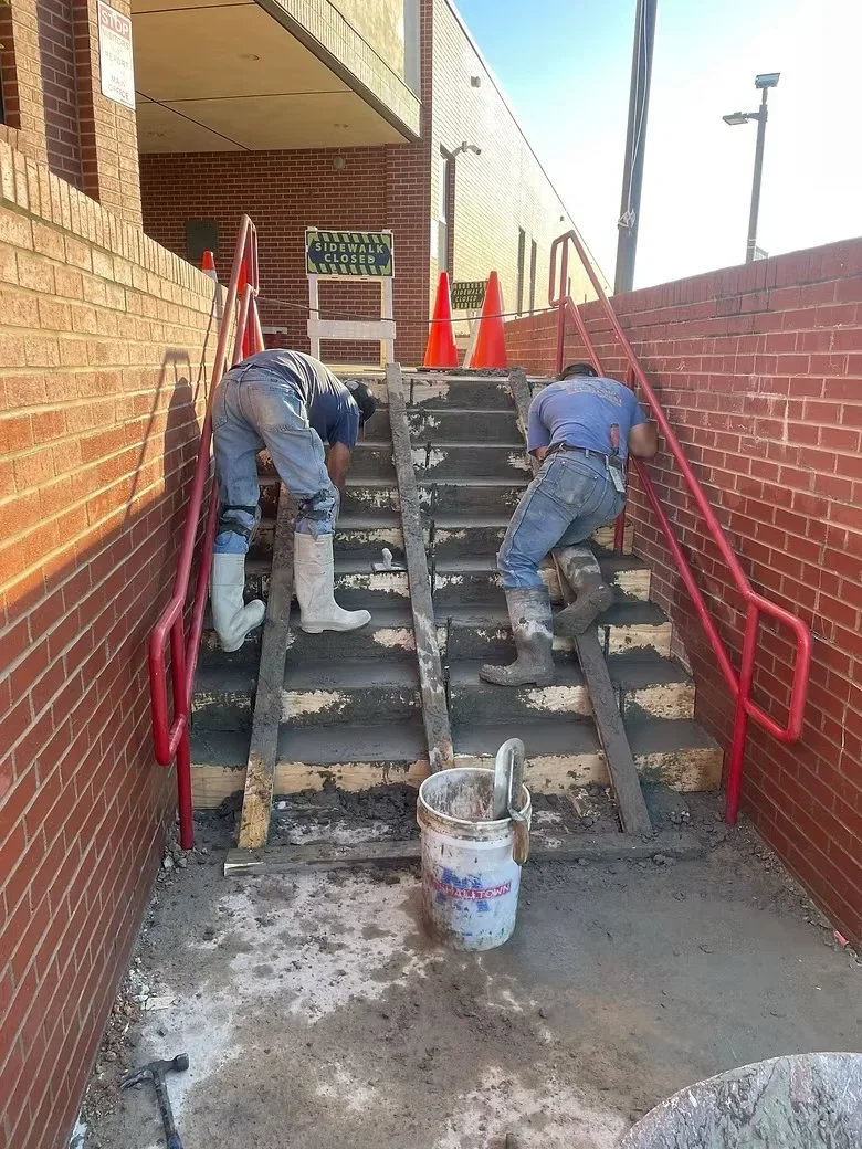 Concrete stair restoration with workers preparing and finishing exterior steps between brick walls