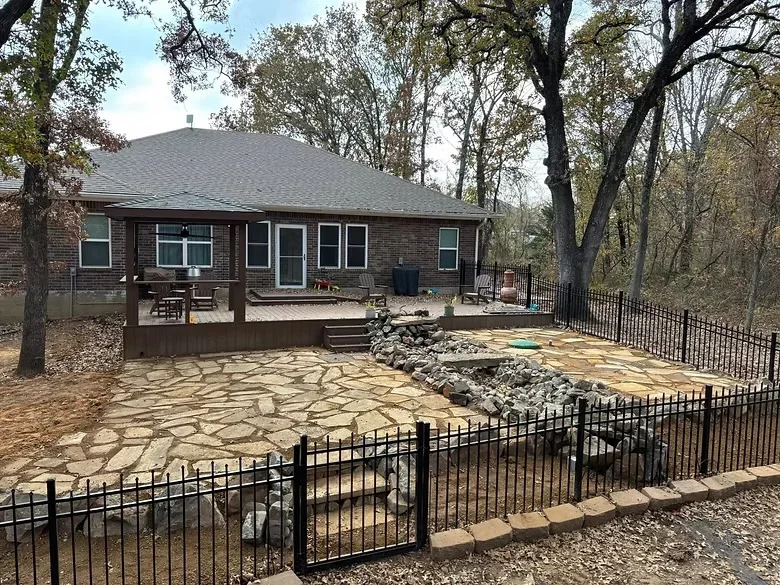 Flagstone patio with irregular stone pattern, black metal fence, and stone edging behind brick home