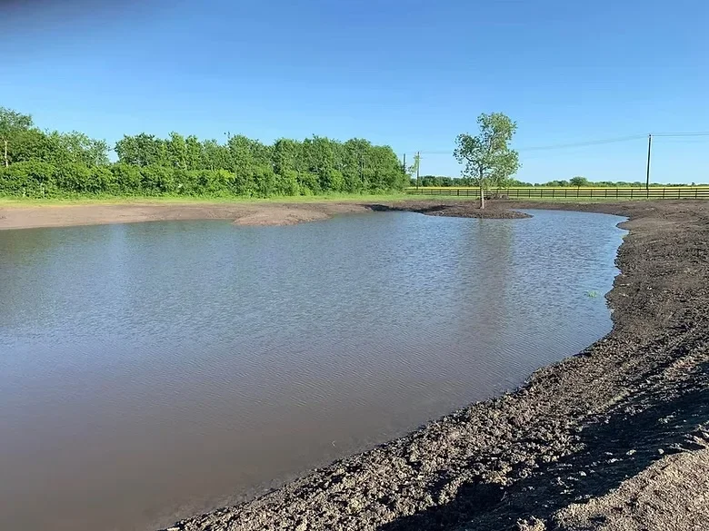Completed livestock pond with concrete work, gravel banks, and metal fencing