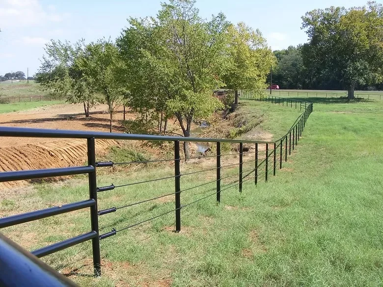 Black metal ranch fencing with horizontal rails and vertical posts installed in pasture with trees