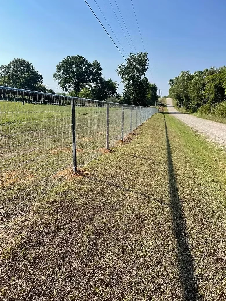 Metal ranch fence with concrete footings along rural driveway and pasture