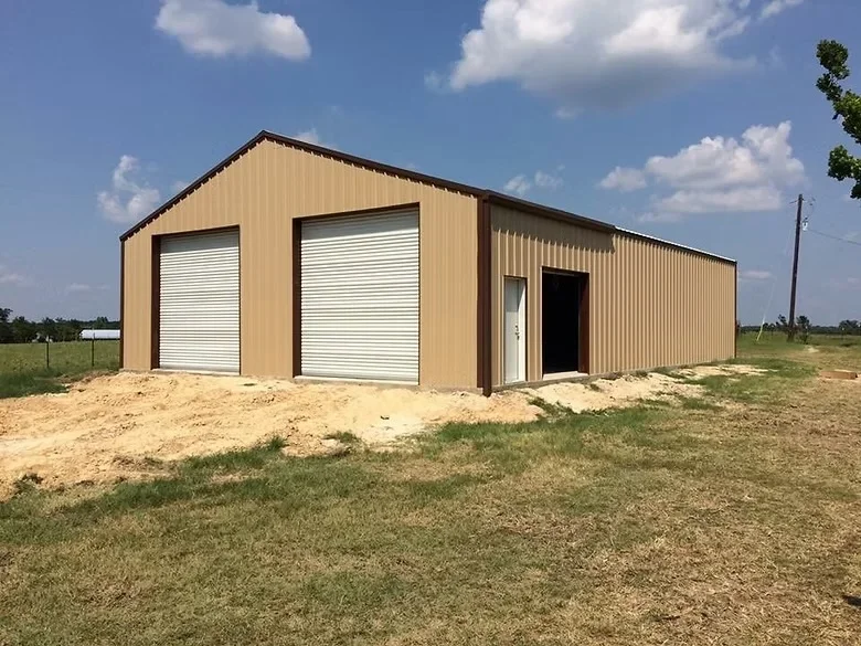 Tan metal building with white roll-up doors and concrete foundation on gravel pad