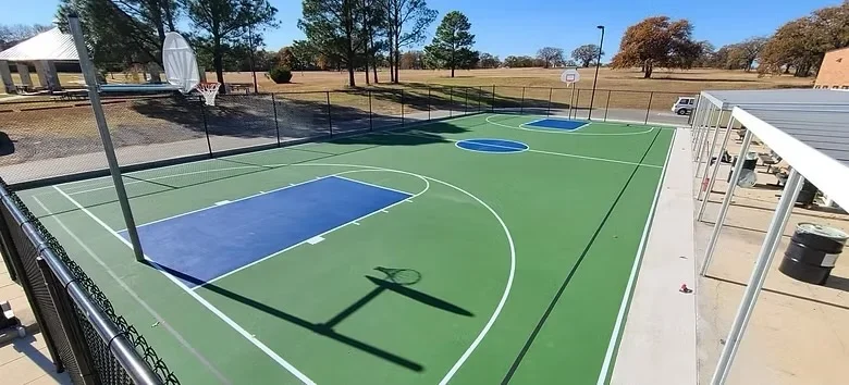 Multi-sport concrete court with blue and green acrylic surface, white court lines, and black net posts