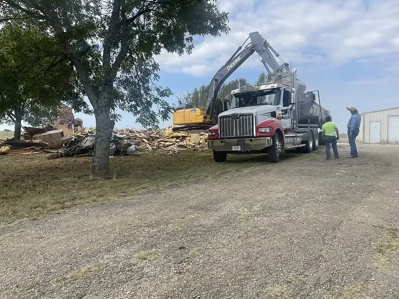 Excavator loading demolition debris onto commercial truck at job site