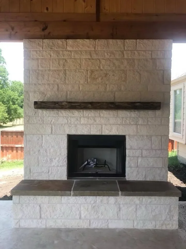 Concrete hearth pad with dark finish beneath stone fireplace with black insert and timber mantel